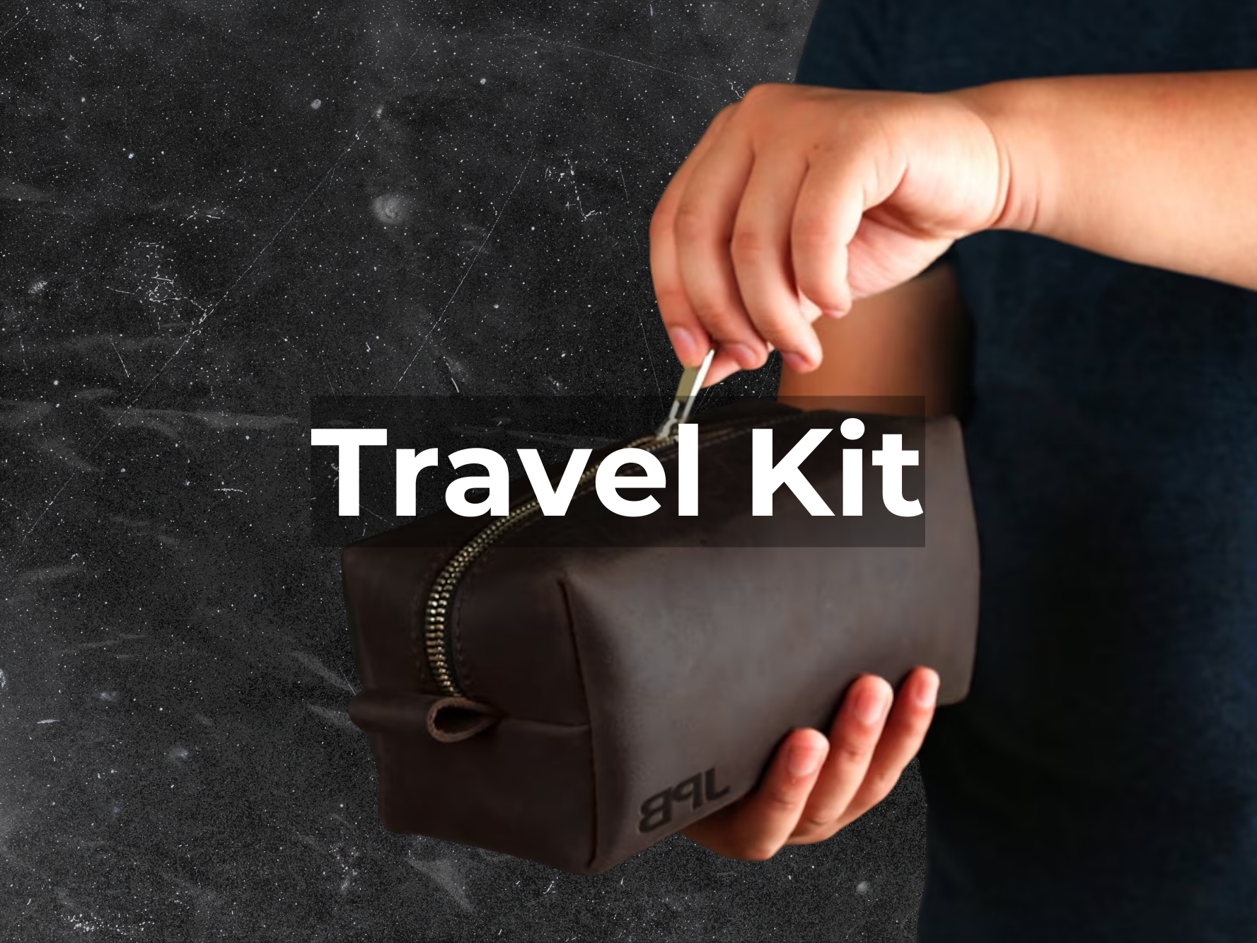 Hand holding a brown leather travel kit with zipper on a dark textured background.